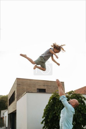 Foto de Padre arrojando al pequeño niño al aire en el jardín. Papá con el niño divirtiéndose al aire libre. Concepto del día de los padres. - Imagen libre de derechos