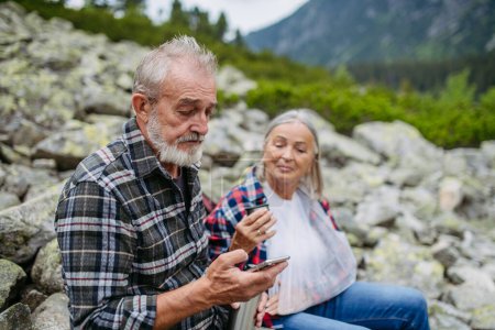 Photo for Senior man calling mountain rescue. A senior woman injured her arm during hike in the mountains. Tourist went off-trail and fell. - Royalty Free Image
