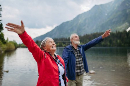 Téléchargez les photos : Tour de taille d'un couple âgé heureux avec les mains en l'air. mari et femme âgés se sentent satisfaits après une randonnée dans les montagnes d'automne. - en image libre de droit