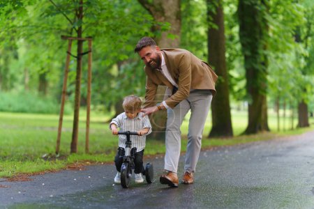 Foto de Padre soltero enseñando a su hijo pequeño a andar en bicicleta en el parque público. Trabajo padre pasar tiempo con el hijo después del día de trabajo. - Imagen libre de derechos