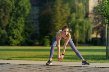 Photo for Full lenght portrait of beautiful fitness woman stretching before outdoor workout in the city park. Healthy lifestyle concept. Copy space. - Royalty Free Image