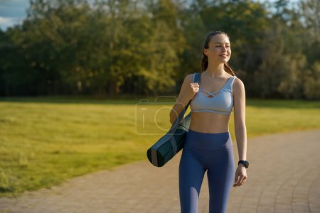 Téléchargez les photos : Portrait de belle fille sportive en vêtements de sport avec tapis de yoga sur la tête de l'épaule pour une séance d'entraînement pilates. - en image libre de droit