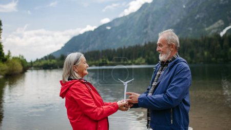 Téléchargez les photos : Portrait d'un couple de personnes âgées tenant un modèle d'éolienne, debout au milieu d'une nature étonnante. Concept d'énergie renouvelable, d'énergie verte et de mode de vie durable. - en image libre de droit