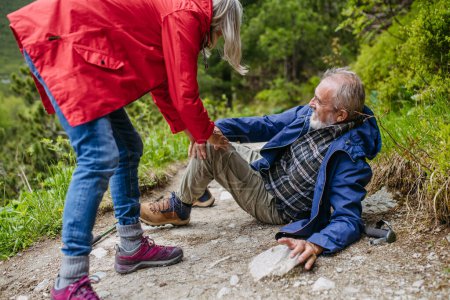 Photo for Senior man injured his leg during hike in the mountains. Tourist went off-trail and fell. Elderly tourist resting on the ground, feeling pain under his kneecap, also known as Hikers knee. - Royalty Free Image