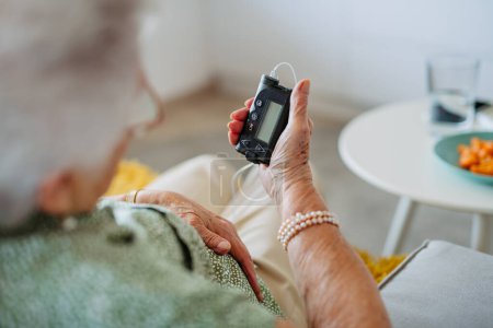 Photo for Close up of diabetic senior patient checking her blood sugar level on insulin pump. Portrait of senior woman with type 1 diabetes taking insuling from tethered insulin pump. - Royalty Free Image
