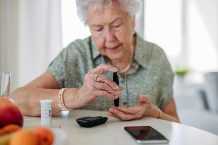 Diabetische Seniorin überprüft ihren Blutzuckerspiegel mit einem Fingerstick-Messgerät. Porträt einer Seniorin mit Typ-1-Diabetes mit Blutzuckermessgerät zu Hause.
