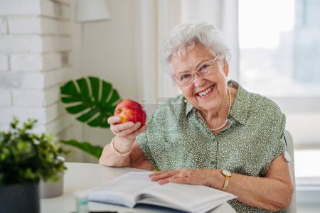Téléchargez les photos : Patients âgés diabétiques utilisant un glucomètre continu pour vérifier leur glycémie à la maison. Femme âgée mangeant des pommes pour aider à élever sa glycémie à la normale. CGM dispositif faisant la vie de la femme âgée - en image libre de droit