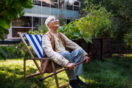 Photo for Portrait of smiling senior man resting after taking care vegetable plants in urban garden. Urban gardening in community garden making pensioner happy and cures his depression. - Royalty Free Image