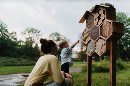 Photo for Mom showing her playful son an insect hotel in public park. A little boy examining bug hotel, looking for bugs, ladybugs or butterflies. - Royalty Free Image