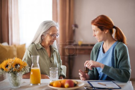 Nurse explaining senior woman how to take medicine. Female caregiver taking care of elderly patient.