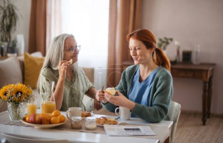 Téléchargez les photos : Infirmière passe du temps de qualité avec une femme âgée à son domicile, prenant un petit déjeuner sain ensemble. Aide-soignante prenant soin d'un patient âgé. - en image libre de droit
