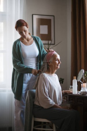 Photo for Nurse spending quality time with senior woman at her home, combing her beautiful hair. Mature woman taking care of her elderly mother. - Royalty Free Image