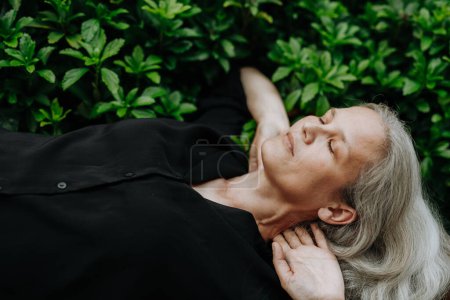 Photo for Shot from above, a beautiful mature woman in middle age with long gray hair, lying on her back with hands behind head and closed eyes. - Royalty Free Image
