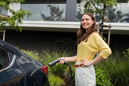 Photo for Close up of beautiful woman plugging charger in her electric car. Progressive woman charging her electric car on the street. Pluging in charger in charging port. - Royalty Free Image