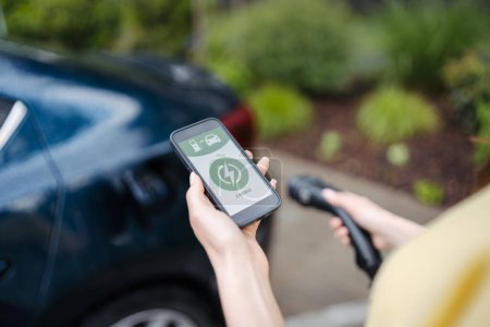 Close up of woman using electric vehicle charging app, checking charging of electric car from smart phone. Charging apps for monitoring electricity usage, locating charging stations.