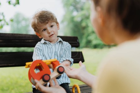 Photo for Single mother with little son playing with wooden toy on park bench. Working parent spending time with son in city park after work day. - Royalty Free Image