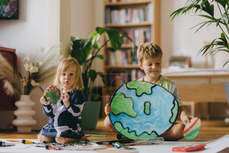 Photo for Siblings painting at home with watercolors and tempera paints, creating a model of planet Earth. A creative project at home during the holidays. A young student preparing a school project on the topic - Royalty Free Image