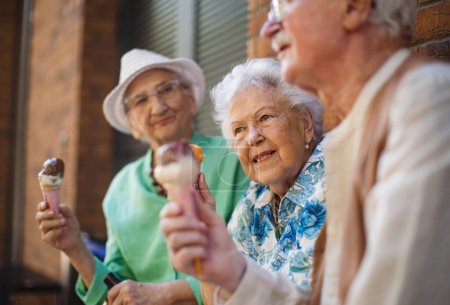 Téléchargez les photos : Portrait de trois amis aînés en ville, mangeant de la crème glacée par une chaude journée d'été. Mesdames âgées en vacances d'été dans la ville. Pensionnés en voyage de groupe. Concept de vacances et de voyages seniors - en image libre de droit
