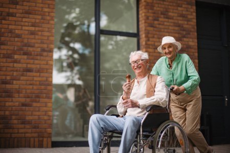 Téléchargez les photos : Portrait de couple de personnes âgées avec un homme en fauteuil roulant. Femme âgée poussant son charmant mari en fauteuil roulant. Concept de maladie chronique chez les couples âgés. Portrait avec espace de copie sur fond noir - en image libre de droit
