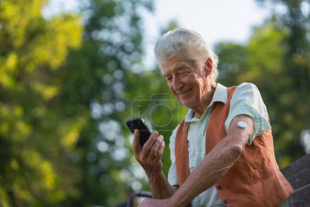 Téléchargez les photos : Homme diabétique senior vérifiant ses données de glucose sur smartphone. Aîné diabétique utilisant un glucomètre continu pour vérifier le taux de sucre dans le sang. - en image libre de droit