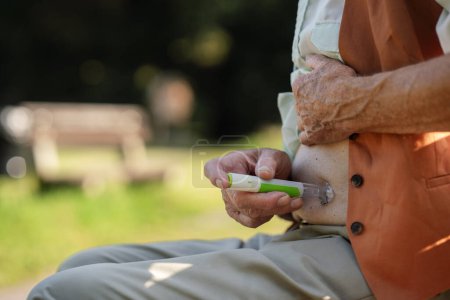 Téléchargez les photos : Patient âgé diabétique injectant de l'insuline dans le ventre à l'extérieur. Gros plan de l'homme âgé atteint de diabète de type 1 prenant isolant avec aiguille à seringue dans le parc de la ville. - en image libre de droit