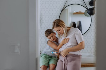 Foto de Mujer inyectándose insulina en el vientre, mientras su hijo la observa y la apoya. Acercamiento de la madre con diabetes tipo 1 que toma insulina con aguja de jeringa. - Imagen libre de derechos