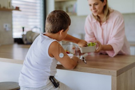 Photo for Diabetic boy with a continuous glucose monitor is careful with his diet. Mother checking what her son with diabetes eating. CGM device making life of school boy easier, helping manage his illness and - Royalty Free Image
