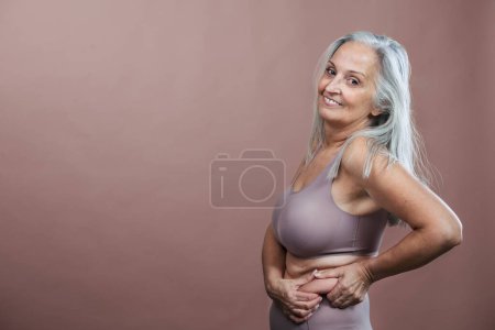 Photo for Portrait of senior woman in a lingerie, studio shoot. Beautiful body shape of aging woman, signs of age on woman body. Isolated on a brown pink background. Copy space. - Royalty Free Image