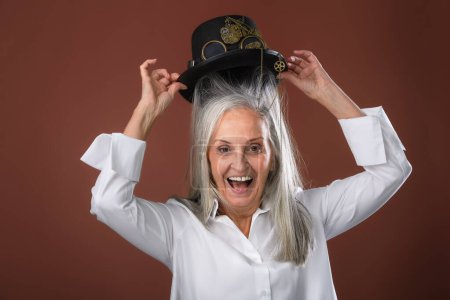Téléchargez les photos : Portrait de femme âgée heureuse dans une chemise mettant un chapeau sur sa tête, tournage en studio. - en image libre de droit