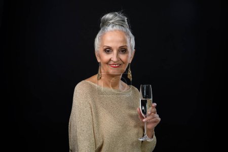 Téléchargez les photos : Portrait de femme âgée bien habillée en tenue de fête tenant un verre de champagne, concept de célébration. Isolé sur fond noir. - en image libre de droit