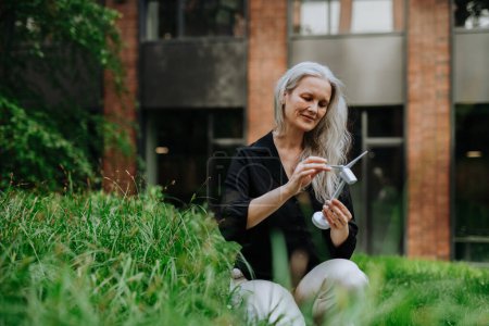 Photo for Portrait of beautiful mature woman in middle age with long gray hair, holding model of wind turbine. Concept of renewable resources. Importance of alternative energy sources and long-term - Royalty Free Image