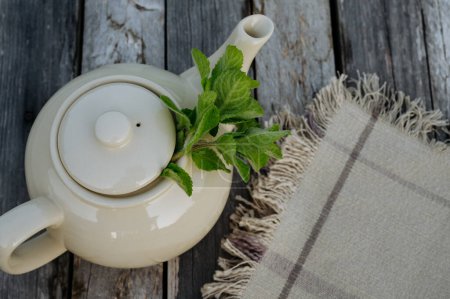 Photo for Top view of a teapot with homemade lemon balm tea on a wooden table. Homegrown herbs are used to prepare herbal tea. Lemon balm as a medicinal herb. - Royalty Free Image