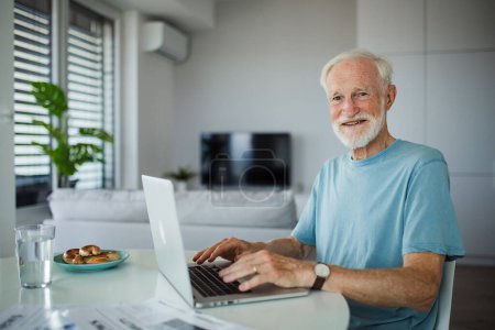 Téléchargez les photos : Homme âgé en fauteuil roulant travaillant à domicile pendant sa retraite. Homme âgé utilisant les technologies numériques, travaillant sur un ordinateur portable. Concept de seniors et compétences numériques. - en image libre de droit