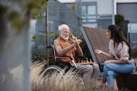 Photo for Senior man playing chess outdoors with his daughter. Nursing home client in wheelchair spending quality time with caregiver, enjoying in a game of chess and conversation. - Royalty Free Image