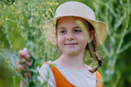 Téléchargez les photos : Portrait d'une jolie petite fille dans un jardin d'automne. La jeune fille en robe et chapeau debout dans l'herbe haute. - en image libre de droit