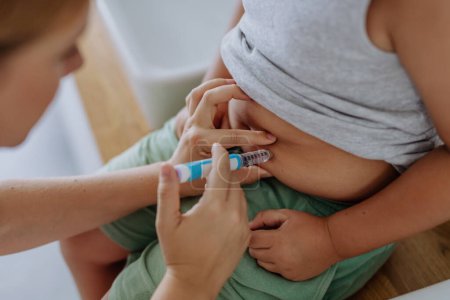 Téléchargez les photos : Mère de garçon diabétique injectant de l'insuline dans son ventre. Gros plan sur un jeune garçon atteint de diabète de type 1 qui prend de l'isolant avec une seringue. - en image libre de droit