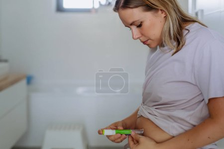 Téléchargez les photos : Femme injectant de l'insuline dans son ventre dans la salle de bain. Gros plan de la mère atteinte de diabète de type 1 prenant isolant avec aiguille de seringue. - en image libre de droit