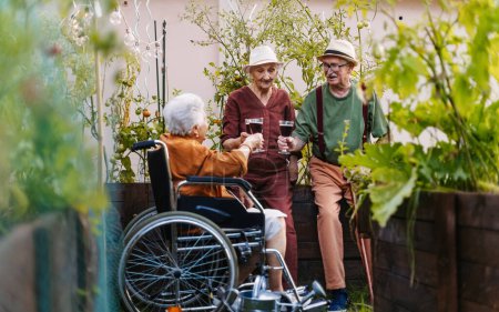 Téléchargez les photos : Portrait d'amis âgés se détendre, boire un verre de vin après avoir travaillé dur dans le jardin urbain de la ville. Les retraités passent du temps ensemble jardinage dans le jardin communautaire dans leur complexe d'appartements. - en image libre de droit