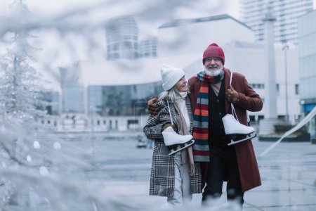 Photo for Portrait of seniors with ice skates at outdoor ice skating rink at the winter. Laughing, embracing each other. - Royalty Free Image