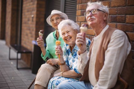 Foto de Retrato de tres amigos mayores en la ciudad, comiendo helado en un caluroso día de verano. Señoras mayores de vacaciones de verano en la ciudad. Pensionistas en viaje de grupo. Concepto de vacaciones y viajes para personas mayores - Imagen libre de derechos