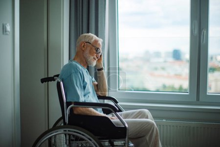 Téléchargez les photos : Un aîné en fauteuil roulant passe du temps seul dans son appartement. Concept de solitude et de dépendance des retraités. - en image libre de droit