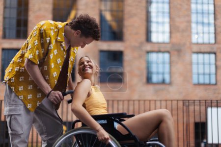 Foto de Hermosa chica de gen Z en una silla de ruedas con su novio. Inclusión, igualdad y diversidad entre la generación Z. - Imagen libre de derechos