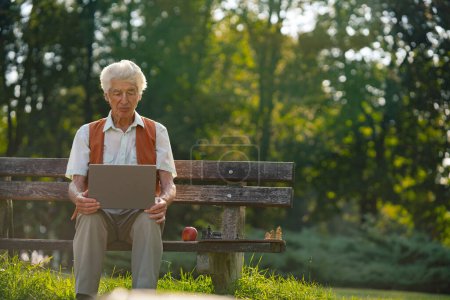 Foto de Hombre mayor sentado afuera y comprando en línea en un portátil. El riesgo de estafas de compras en línea dirigidas a las personas mayores. - Imagen libre de derechos