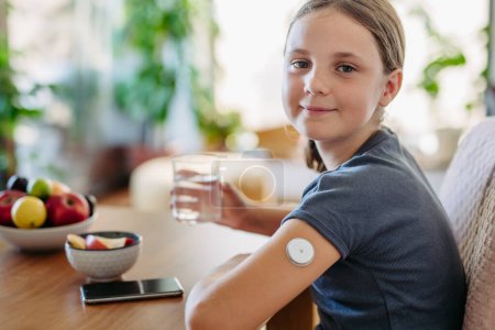 Photo for Close up of continuous glucose monitor sensor on girls arm. Girl drinking water to better manage her diabetes. - Royalty Free Image