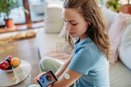 Photo for Woman with diabetes using continuous glucose monitor. Diabetic woman connecting CGM to a smartphone to monitor her blood sugar levels in real time. - Royalty Free Image