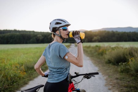 Téléchargez les photos : Cycliste diabétique avec un glucomètre continu sur son bras boire de l'eau pendant sa tournée à vélo pour gérer son diabète tout en faisant de l'exercice. Concept d'exercice et de diabète. - en image libre de droit