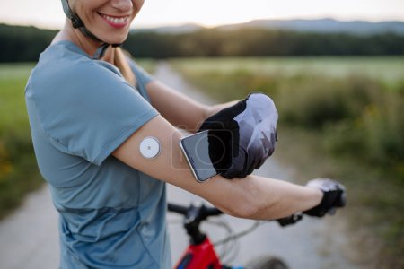 Photo for Diabetic cyclist connecting continuous glucose monitor with her smartphone to monitor her blood sugar levels in real time. Concept of exercise and diabetes. - Royalty Free Image