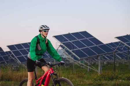 Foto de Retrato de un hermoso ciclista cabalgando frente a paneles solares en una granja solar durante un recorrido en bicicleta de verano en la naturaleza. Una granja solar como solución para un futuro energético más sostenible. - Imagen libre de derechos
