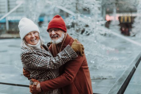 Photo for Portrait of seniors in winter at outdoor ice skating rink. Smiling, embracing each other. - Royalty Free Image