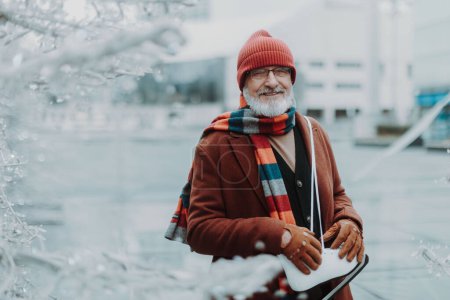 Photo for Portrait of happy senior man in winter at an outdoor ice skating rink. Elderly man holding brand new ice skates. - Royalty Free Image